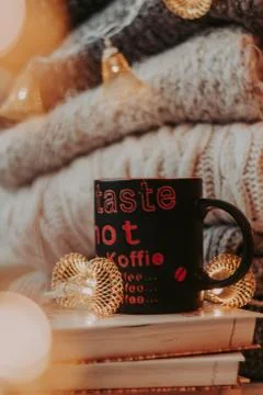 A pile of sweaters, a stack of old books, a beautiful black and red cup, ligh Stock-Fotos
