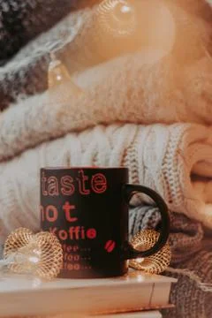 A pile of sweaters, a stack of old books, a beautiful black and red cup, ligh Stock Photos