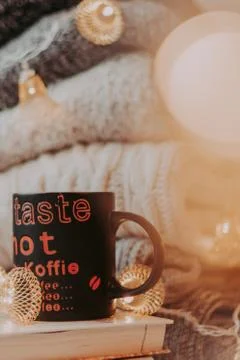 A pile of sweaters, a stack of old books, a beautiful black and red cup, ligh Stock Photos
