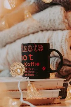 A pile of sweaters, a stack of old books, a beautiful black and red cup, ligh Stock-Fotos