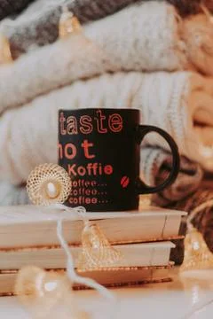 A pile of sweaters, a stack of old books, a beautiful black and red cup, ligh Stock Photos