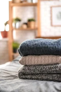 Pile of three knitted sweaters on bed. Stock Photos