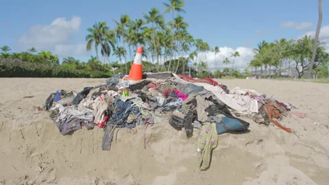A pile of trash, clothes, empty bottles and traffic cone sitting on a beach in Stock Footage 264078974