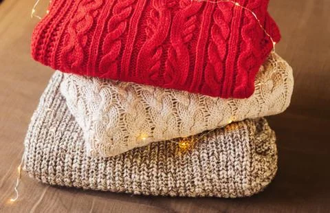 A pile of warm sweaters on the tissue background decorated with lights. Foto stock