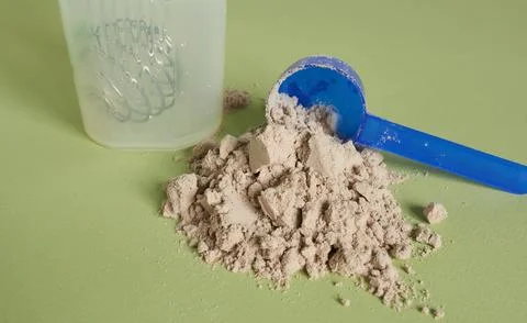 Pile of whey protein powder with scoop on green background. Stock Photos