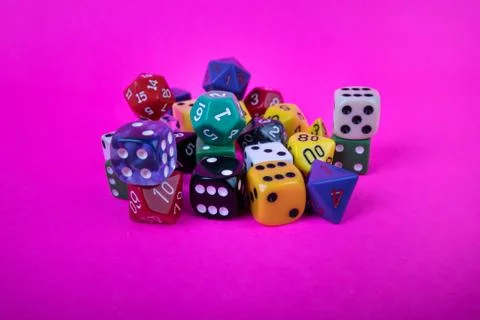 Piled up game dice random sizes and colors on bright pink background Stock Photos
