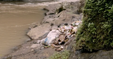 Piles of garbage thrown by the side of a river with offerings in Bali Stockbeeldmateriaal 87794108