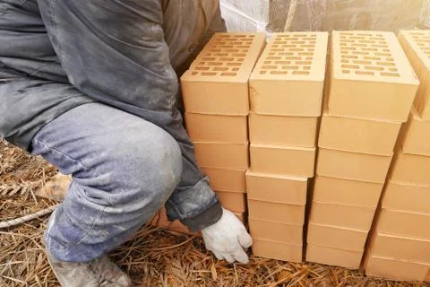 Piles of orange bricks, stacked in rows, the worker carries several pieces. Stockfoto's