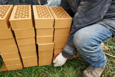 Piles of orange bricks, stacked in rows, the worker carries several pieces. Stockfoto's