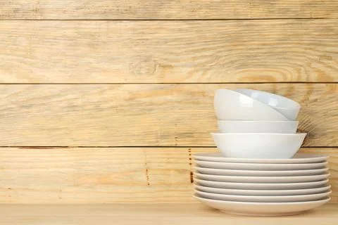 Piles of white ceramic tableware, plates, saucers and cups on a natural woode Stock Photos