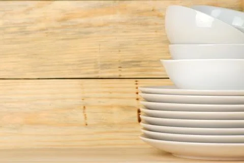 Piles of white ceramic tableware, plates, saucers and cups on a natural woode Stock Photos