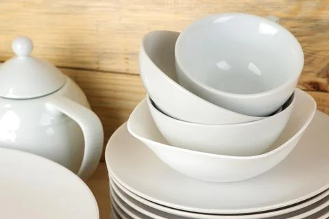 Piles of white ceramic tableware, plates, saucers and cups on a natural woode Stock Photos