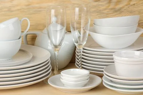 Piles of white ceramic tableware, plates, saucers and cups on a natural woode Stock Photos