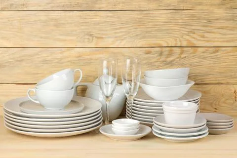 Piles of white ceramic tableware, plates, saucers and cups on a natural woode Stock Photos