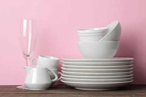 Piles of white ceramic tableware, plates, saucers, cups on a pink background. Stock Photos