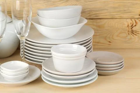 Piles of white ceramic tableware, plates, saucers and cups on a natural woode Stock Photos