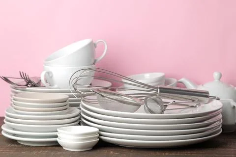 Piles of white ceramic tableware, plates, saucers, cups on a pink background. Stock Photos