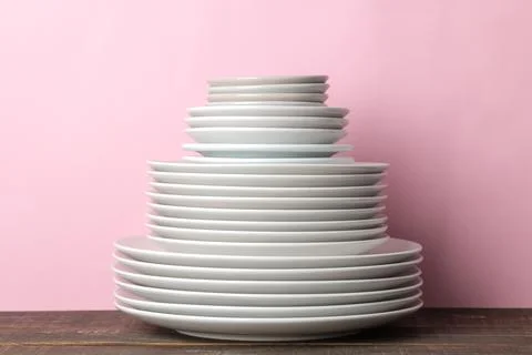 Piles of white ceramic tableware, plates, saucers, cups on a pink background. Stock Photos