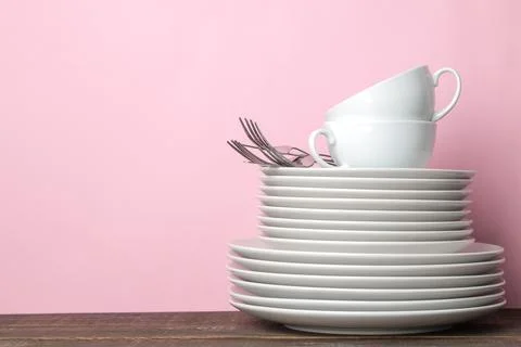 Piles of white ceramic tableware, plates, saucers, cups on a pink background. Stock Photos