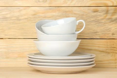 Piles of white ceramic tableware, plates, saucers and cups on a natural woode Stock Photos