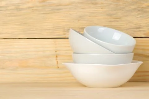 Piles of white ceramic tableware, plates, saucers and cups on a natural woode Stock Photos