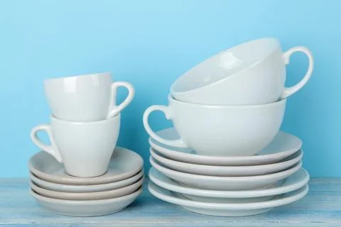 Piles of white ceramic tableware, saucers and cups on a gentle blue backgroun Stock Photos