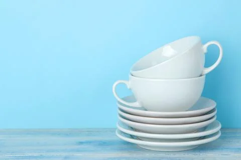 Piles of white ceramic tableware, saucers and cups on a gentle blue backgroun Stock Photos