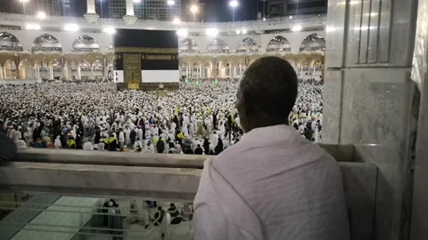 Pilgrims pray while looking at the Kaaba while other pilgrims surround the Kaaba Stock Footage 130228895