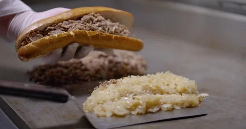 Piling chopped steak and onions into a long roll, creating a Philly cheesesteak Stock Footage 85042476