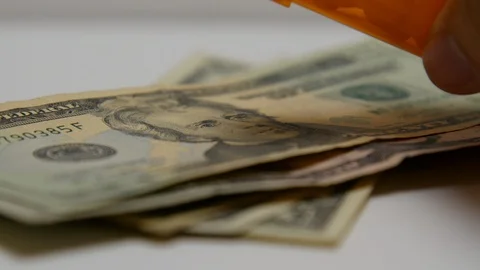 Pill bottle pours out white pills onto stacks of money. Stock Footage 108032891