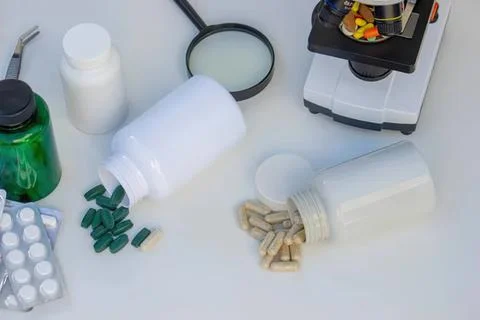 Pill bottles and capsules with a microscope on white table Stock Photos