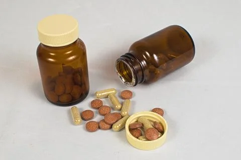 Pill bottles next to various tablets and capsules Stock Photos
