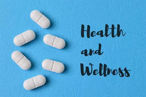 Pill capsules on blue background with text HEALTH and WELLNESS Stock Photos