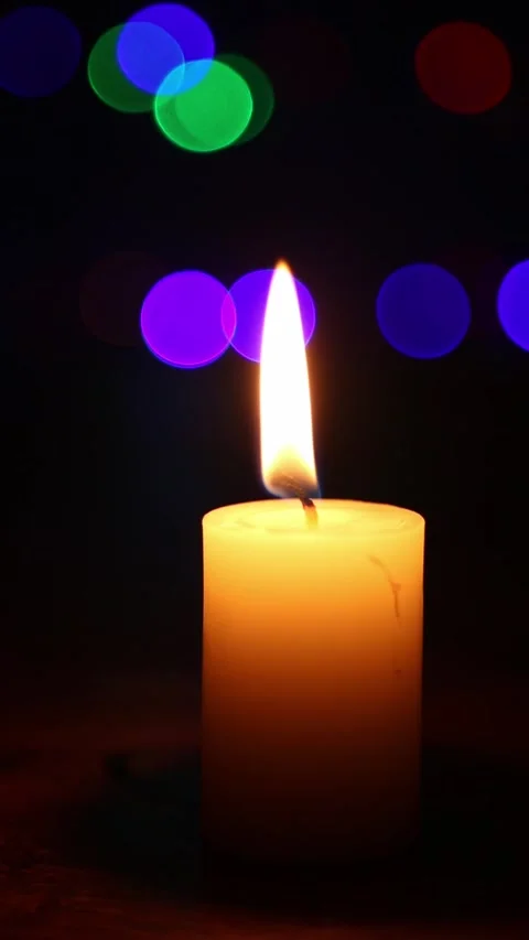 Pillar candle flame flickering against colorful bokeh lights at night Video stock 340383106