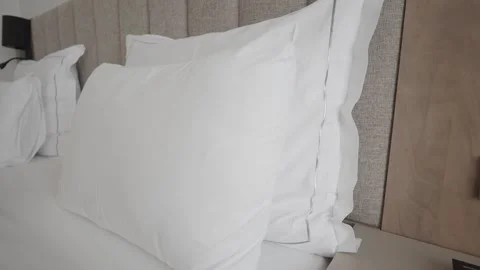 Pillows on a bed with a bedside panel and light switch in a modern room Stock Footage 346270413