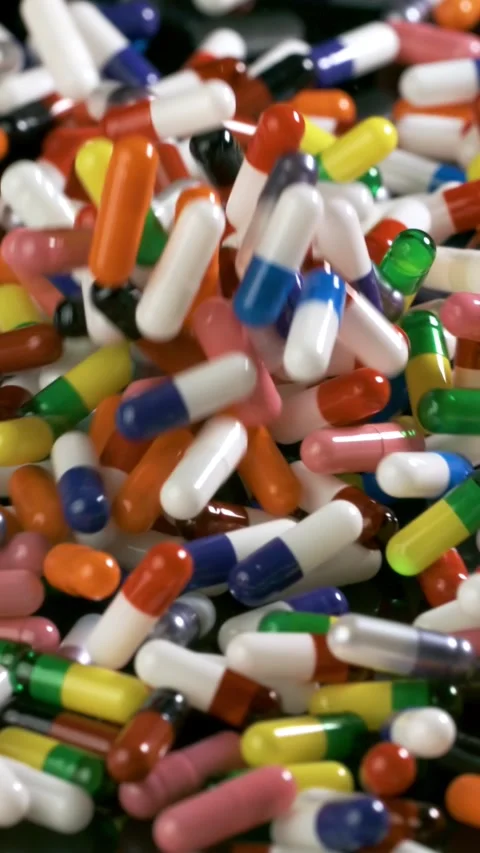 Pills and pill bottle fall onto a black surface in slow motion. Vertical Video. Stock Footage 320580619