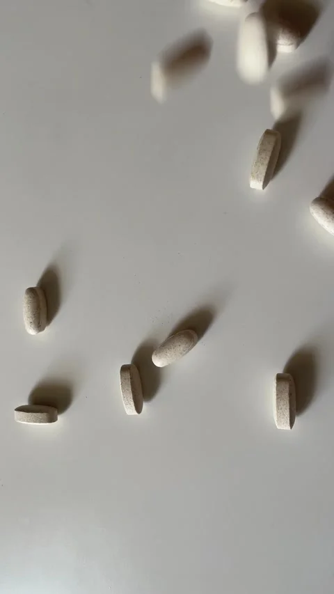 Pills and Supplements Falling onto White Table Surface in Slow Motion Stock Footage 340214694