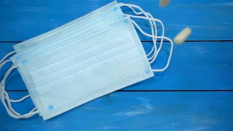 Pills fall in slow motion on a surgical mask on a blue Stock Footage 136568325