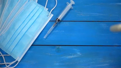 Pills fall in slow motion on a surgical mask and syringe on a blue Vídeo Stock 136568406