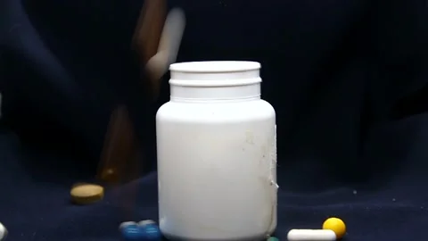 Pills falling around a white jar on a black background Stock Footage 337427131