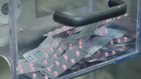 The pills filled and packaged in blister pack are falling down to the container Stock Footage 199686676