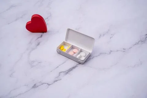 Pills inside a pillbox on a table, next to a red heart .Health concept. Stock Photos