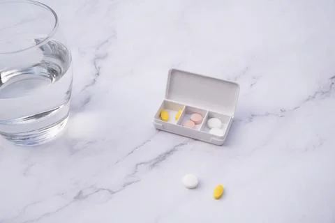 Pills inside a pillbox on a table, next to a glass of water. Health concept. Stock Photos