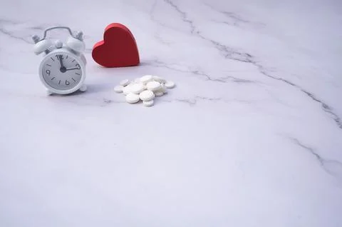 Pills next to a clock and a red heart on a table,  remainding the time to t.. Stock Photos