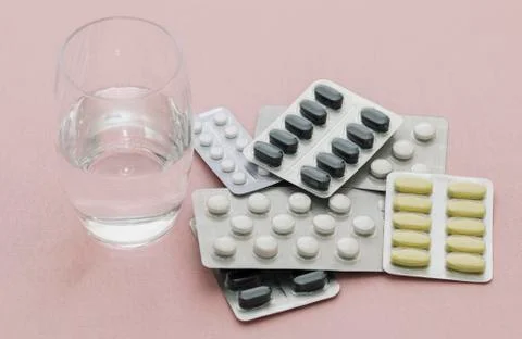 Pills in the package are on the table with a glass of water, pink background Stock Photos