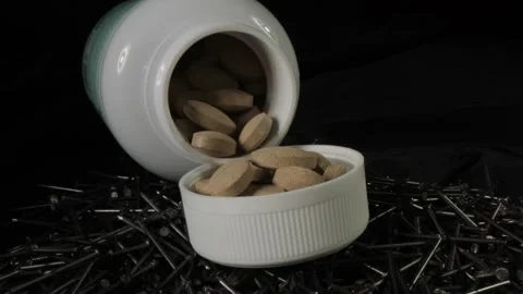 Pills spilling out of pill bottle on metal nails on black background. The Stock Footage 265467936