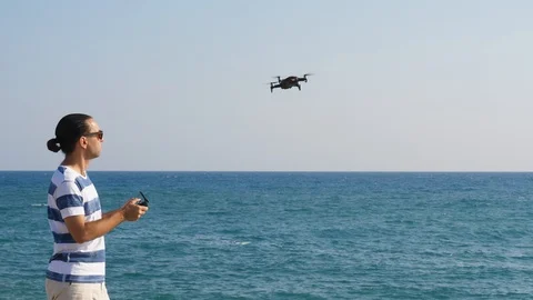 Pilot guy launch small quadcopter to fly over sea. Man stand at sunny beach Stock Footage 105198856