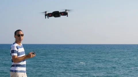Pilot man control little drone flying towards camera, sunny outdoors at sea Video stock 105198971