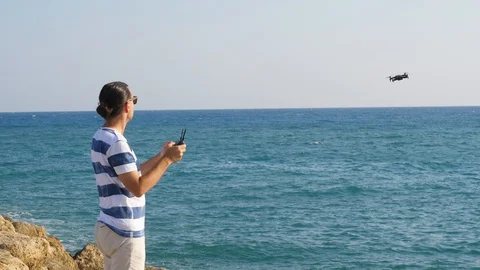 Pilot man controlling small quadcopter, aircraft fly back from sea Stock Footage 105198759