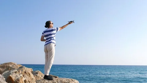 Pilot man stretch out hang and land little drone on it, sunny sea beach area Stock Footage 105199111